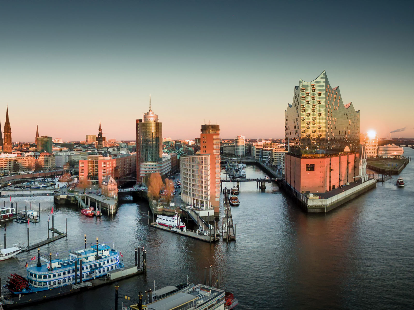 Das Titelbild zum Beitrag "Entwicklung der Baubranche in der Metropolregion Hamburg" zeigt die Stadt aus Richtung der Elbe bei Sonnenaufgang.