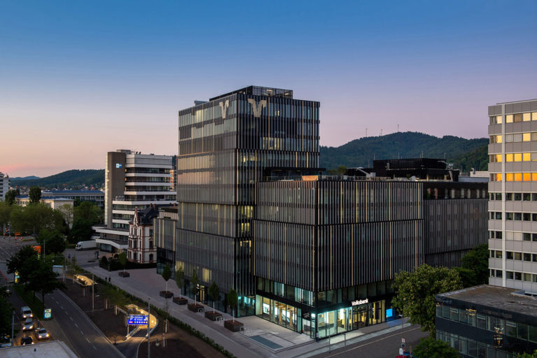 Das blockartige, dunkle Gebäudeensemble in der Bismarckallee 10 in Freiburg während der Dämmerung.