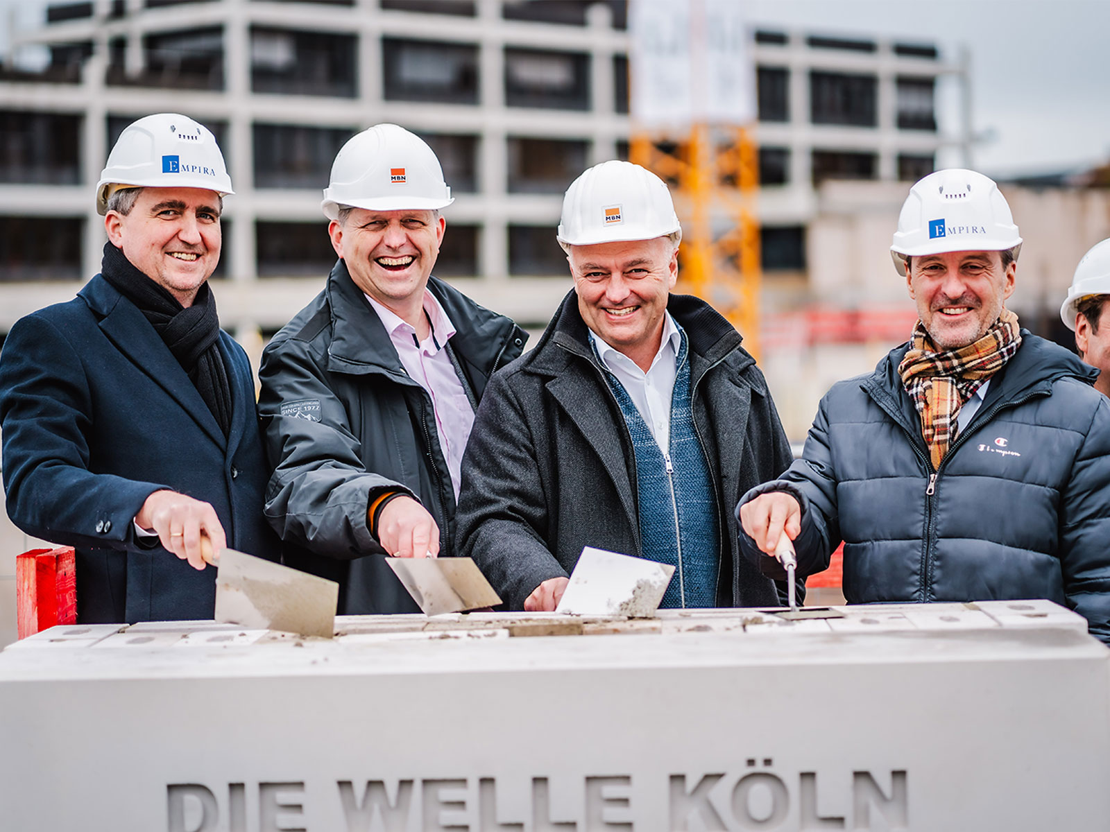 4 Männer stehen hinter dem Grundstein des Naubaus "Die Welle Köln".