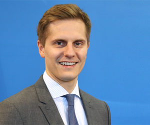 Protrait von Dr. Benjamin Grimm. Lächelnder, braunhaariger Mann mit Anzug und dunkelblauer Krawatte.