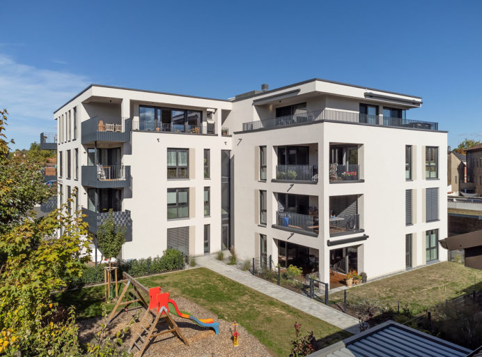 Foto des Friedrich-Ebert-Carré in Kitzingen. Ein Kleiner Spielplatz liegt vor dem 4-stöckigen Wohnhaus.