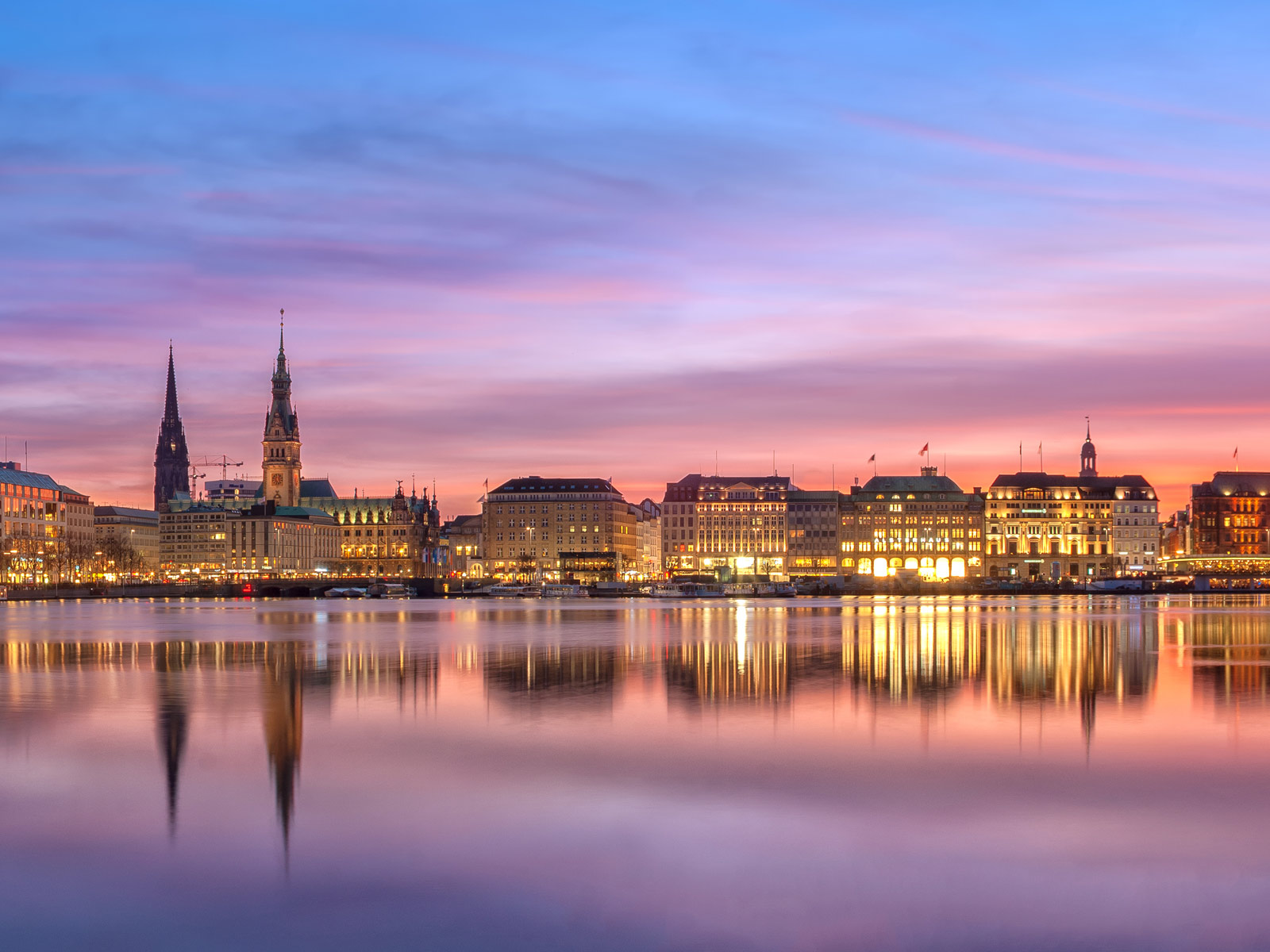 Hintergrundbild zum Beitrag Werkstattverfahren Hamburg: Die Stadt von der Binnenalster aus im Sonnenuntergang. Beleuchtete Gebäude spiegeln sich im Wasser.