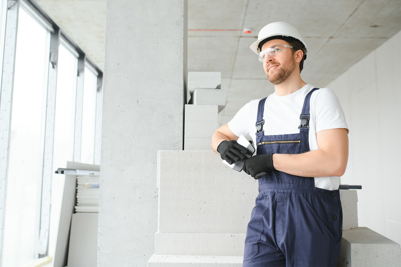 Auf dem Profilbild von Hansa Bautenschutz aus Hamburg lehnt sich ein junger Handwerker mit Latzhose, Helm und Handschuhen auf einen Betonklotz