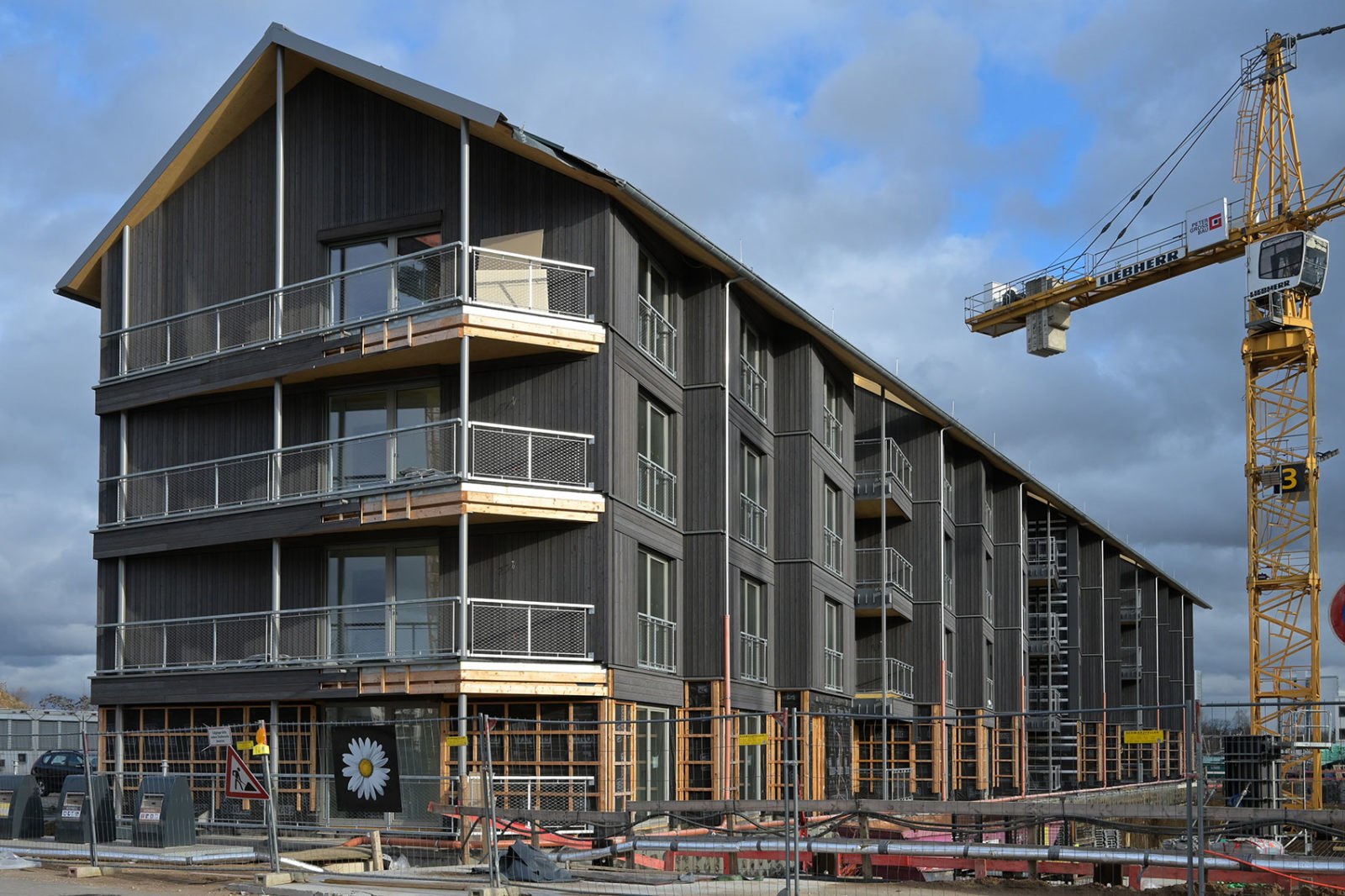 Bild des Holzhybridhaus im neubaugebiet Mannheim Franklin. Das Mehrfamilienhaus hat eine sehr dunkle Holzfassade und ein Spitzdach.