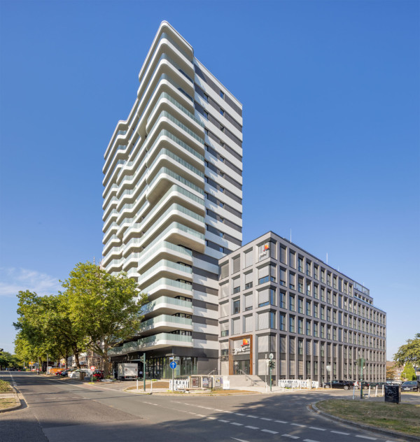 Visualisierung des Huyssen Quartier in Essen: Ein moderner Wohnturm mit abgerundeten Ecken und hervorstehenden Balkonen. Daneben steht ein modernes Bürogebäude.