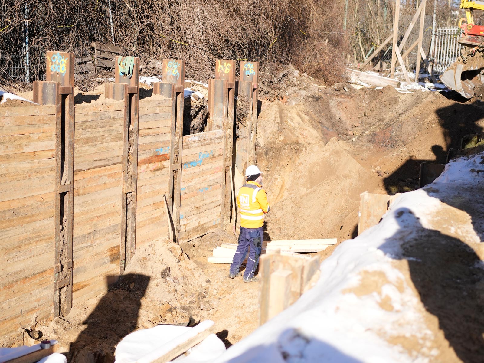 Ein Mitarbeiter der IN-SCHAAT GmbH steht in einer Baugrube, die mit Stützwänden aus Holz abgesichert wurde