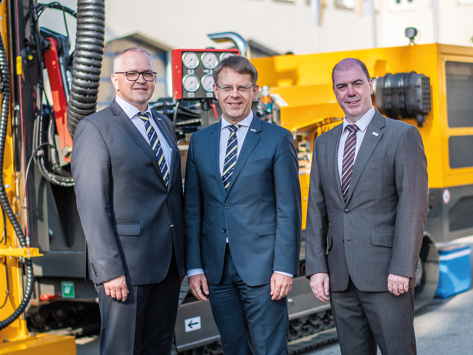 Die Geschäftsführung der KLEMM Bohrtechnik GmbH (drei Männer in Anzügen) stehen vor einem Bohrgerät.