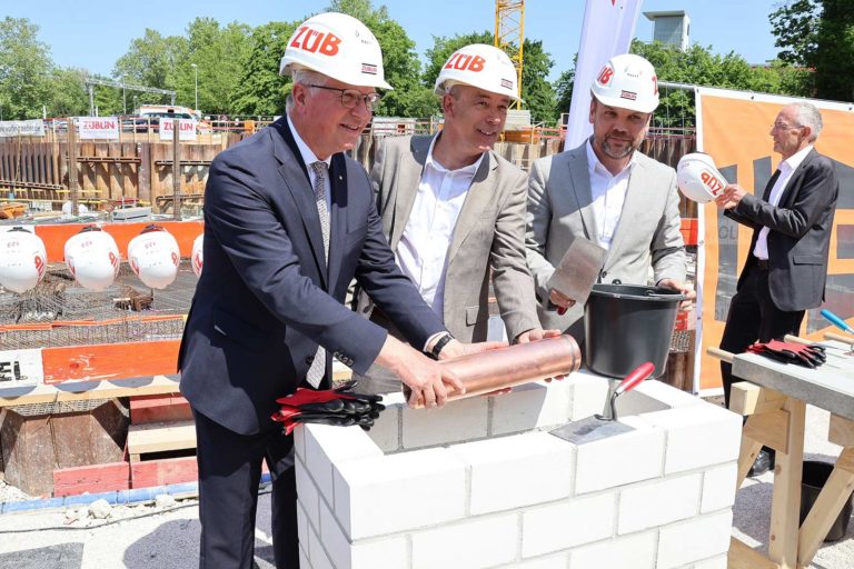 Grundsteinlegung Landratsamt Esslingen: 3 Männer tragen Helme mit der Aufschrift "Züblin" und halten eine Zeitkapsel.