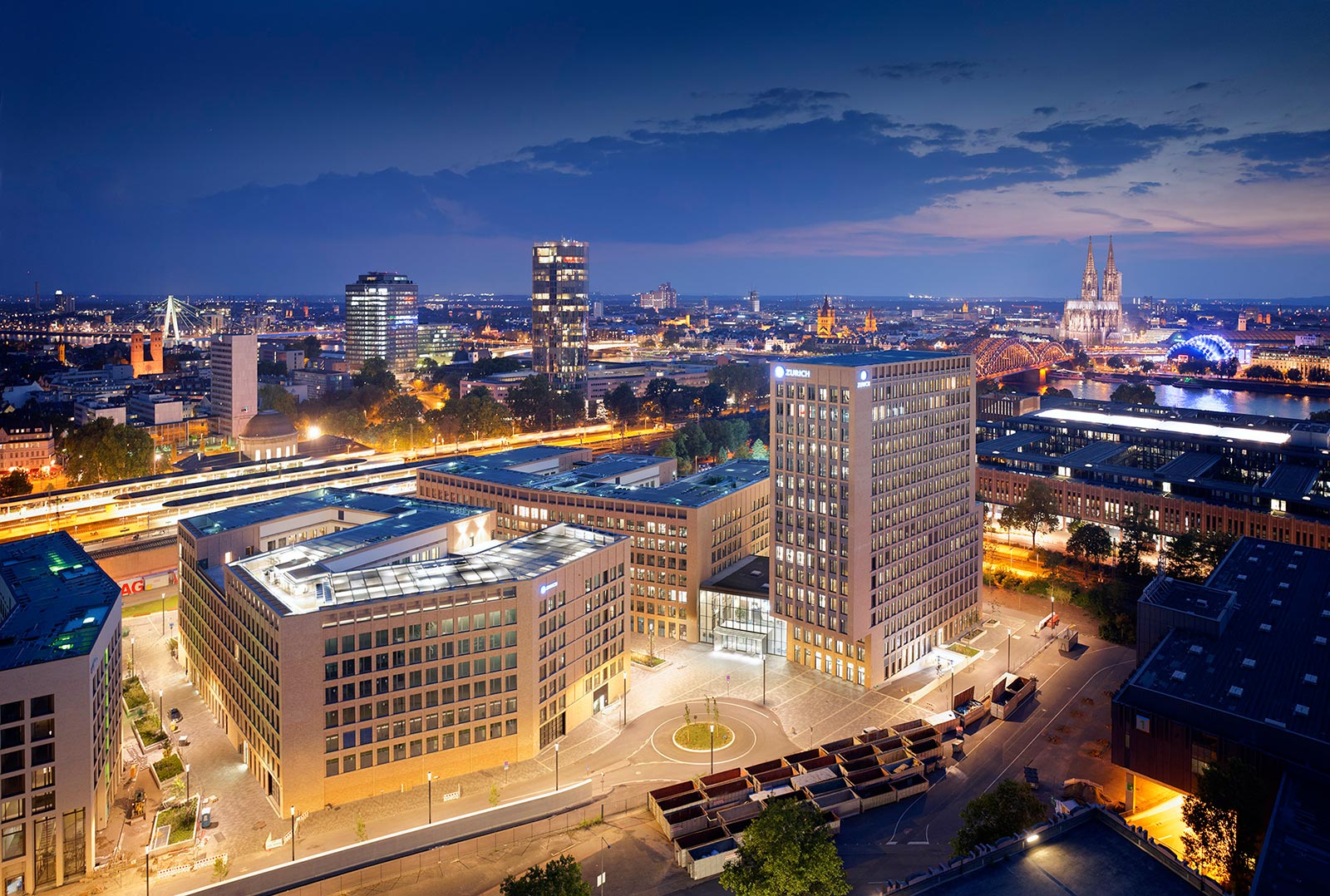 Die fertigen und beleuchteten Gebäude der MesseCity Köln bei Dunkelheit. Köln im Hintergrund