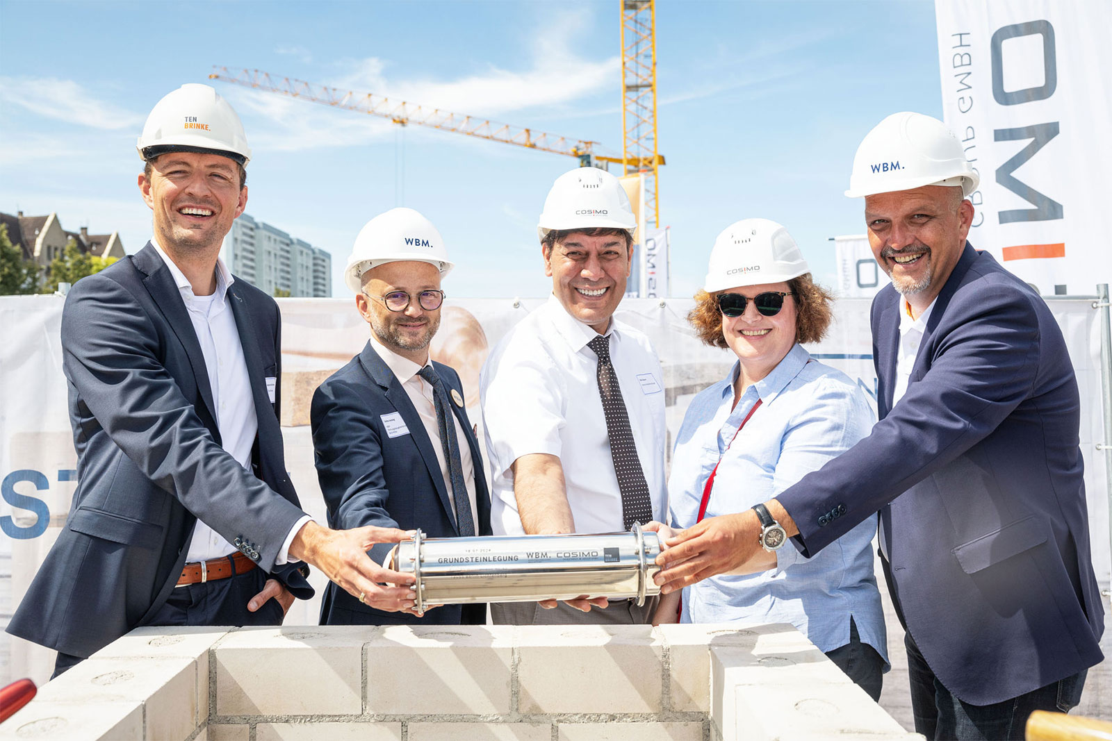 Fünf Personen halten bei der Frundsteinlegung für den Neubau an der Konrad-Wolf-Straße in Berlin eine Zeitkapsel