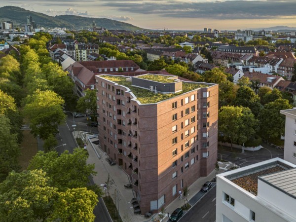 Rennwegdreieck: 8-stöckiges, dreieckiges Wohnhaus mit Klinkerfassade mitten im begrünten Freiburg. Berge im Hintergrund