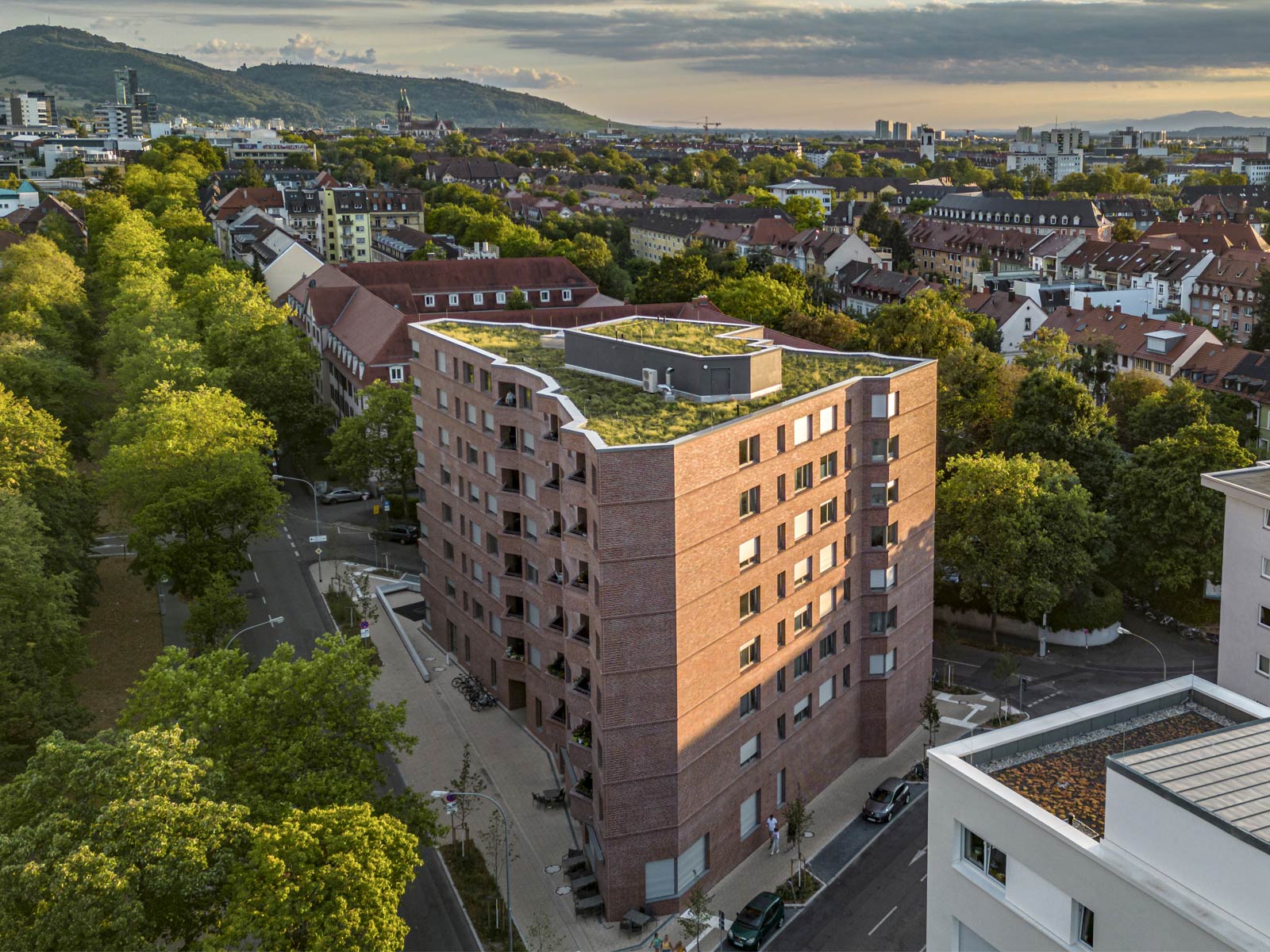 Rennwegdreieck: 8-stöckiges, dreieckiges Wohnhaus mit Klinkerfassade mitten im begrünten Freiburg. Berge im Hintergrund