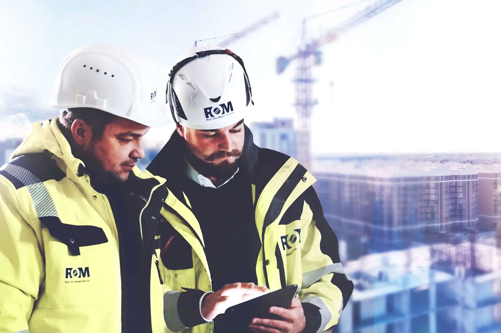 Zwei Männer mit weißen Bauhelmen und in neongelben Jacken mit der Aufschrift ROM Rud. Otto Meyer Technik