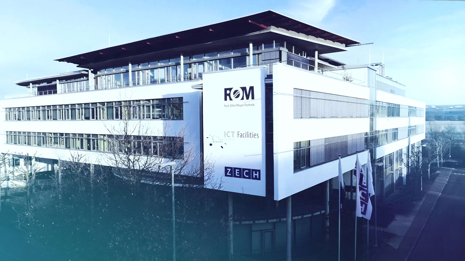 Firmengebäude von ROM Technik von außen. Im Vordergrund sind Firmenlogos auf der Fassade zu sehen