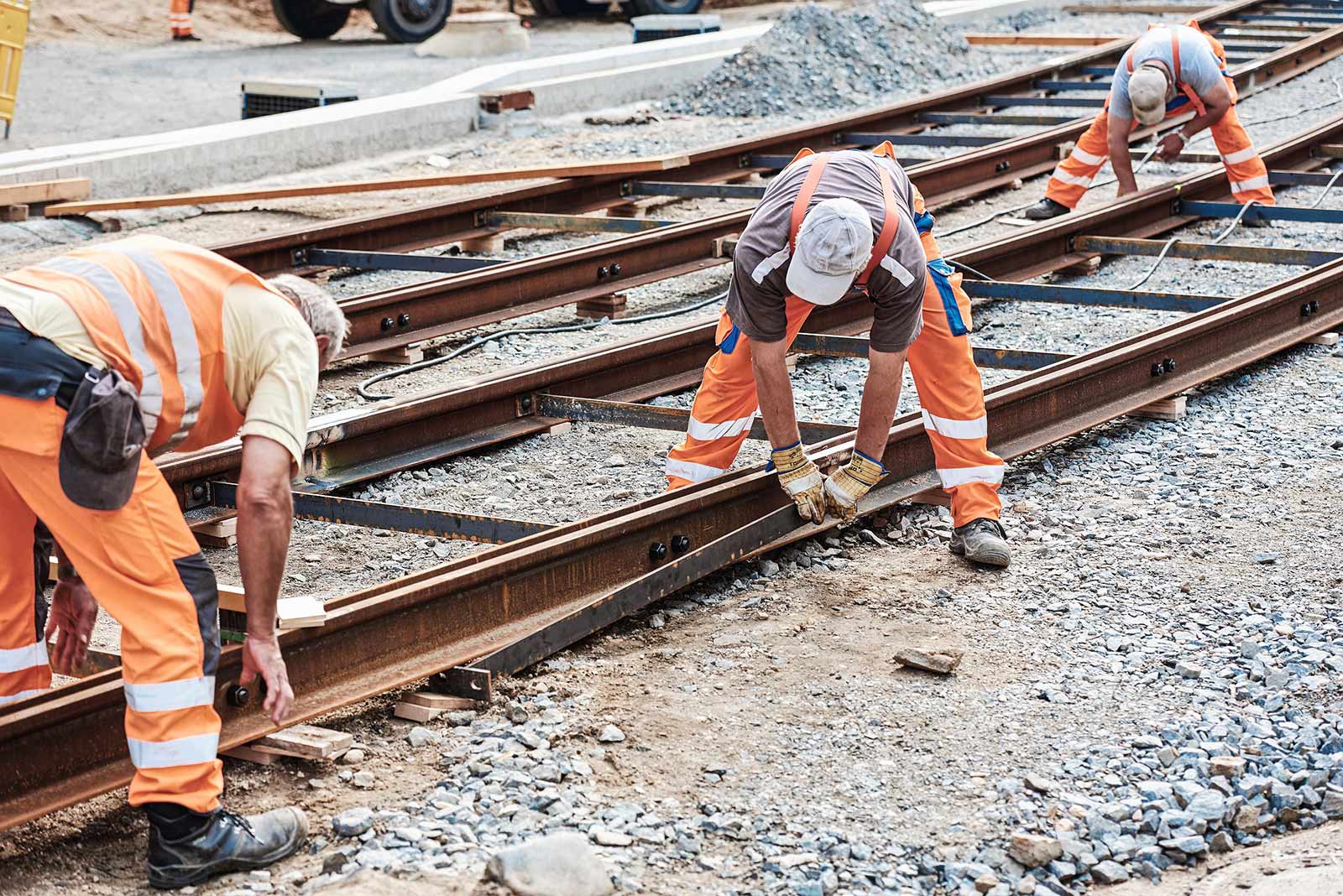 Drei Mitarbeiter der STRABAG AG arbeiten bückend an einem Bahngleis.