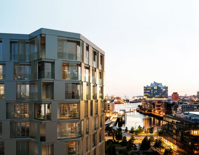 Visualisierung von THE LYTE im Westfield Hamburg-Überseequartier. Das polygone gebäude ist links im Bild, rechts im Hintergrund der Ausblick auf den Hafen und die Elbphilharmonie bei Sonnenuntergang.