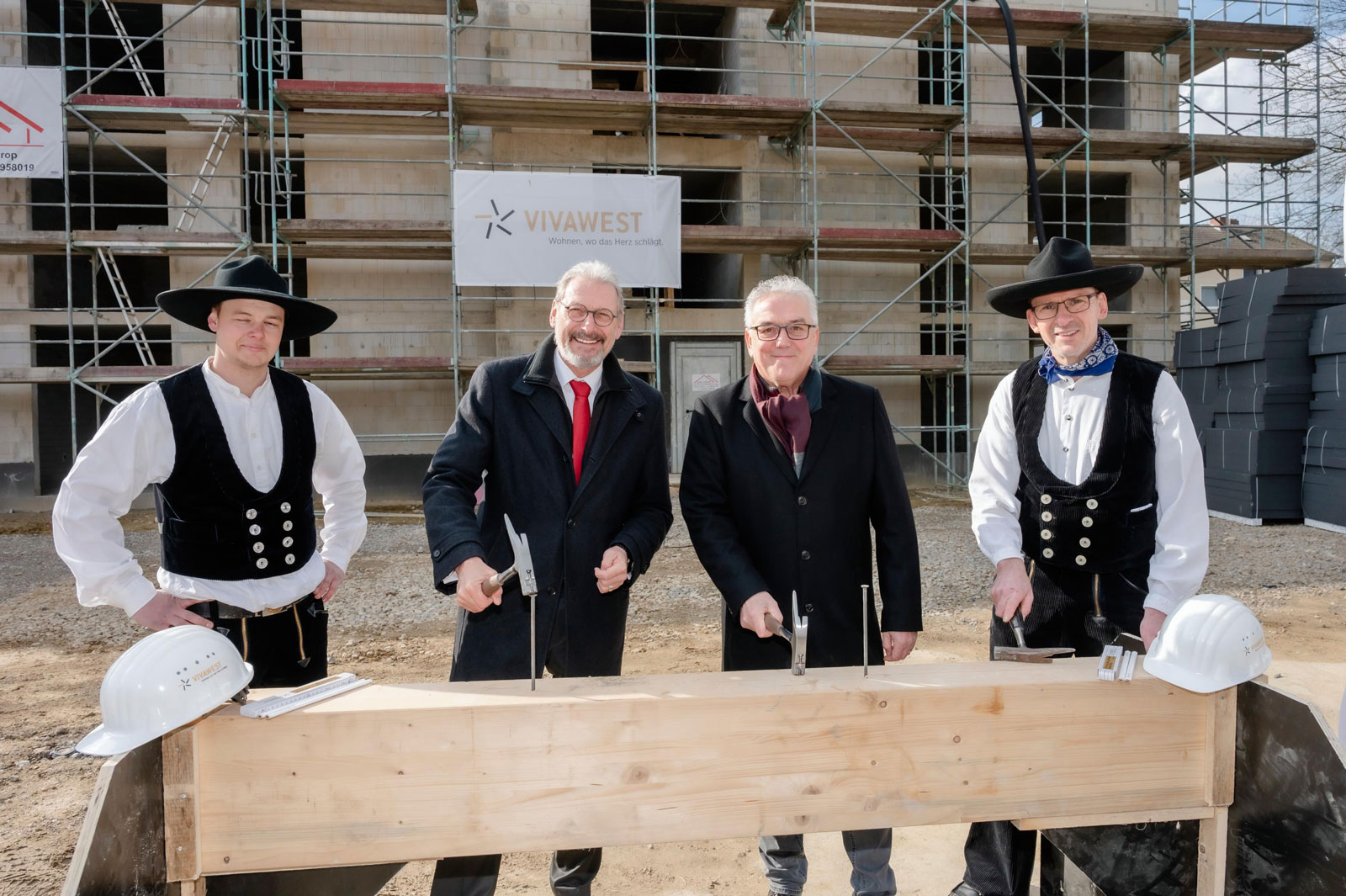 Vivawest feiert Richtfest für den Neubau an der Zillestraße in Oer-Erkenschwick. Vier Männer in Anzügen und traditioneller Zimmermannskleidung lachen in die Kamera.