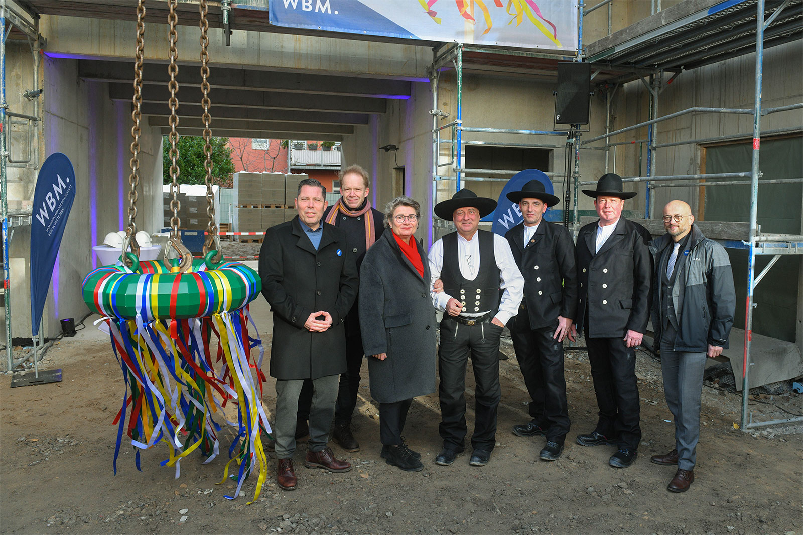 Sechs Personen stehen beim Richtfest des Neubaus der WBM an der Bernauer Straße Berlin neben einem Richtkranz.